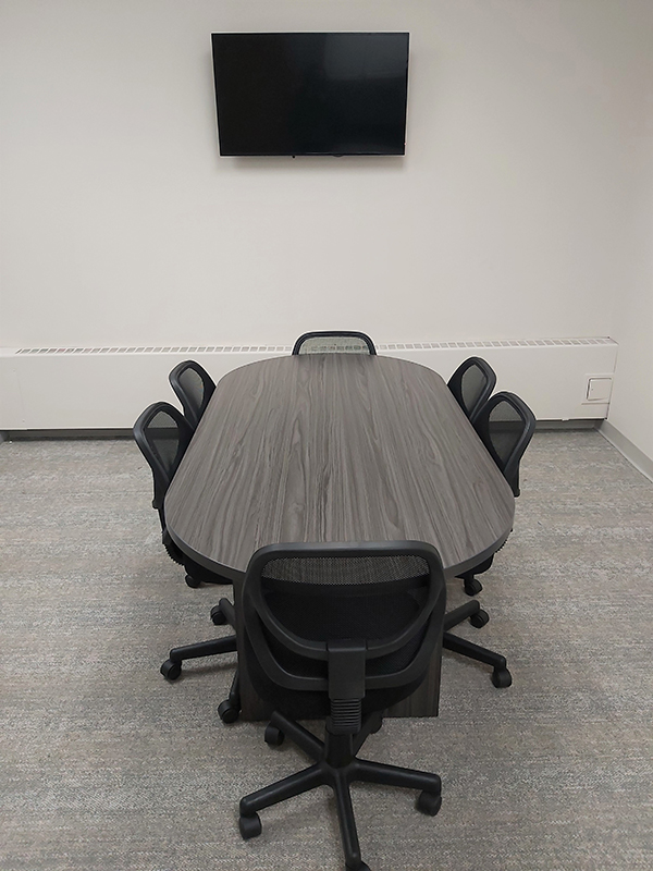 Two desks with computer monitors and a bookshelf in the corner of a room with maps on the two walls.