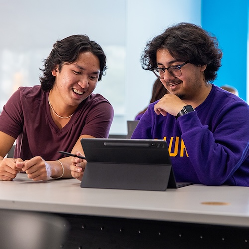 Two students sitting at a desk looking at a tablet together