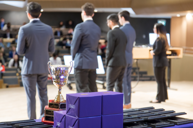 student team presenting on stage with trophies in foreground