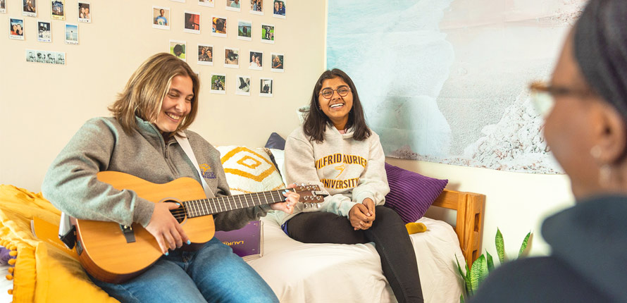 three female students playing guitar in residence room