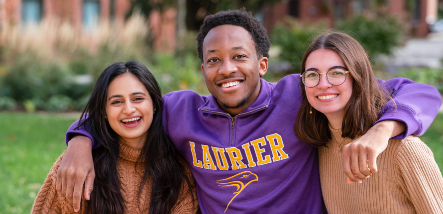 three students sitting closely together and smiling