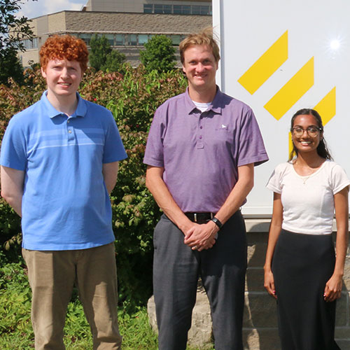 Three people standing in front of a sign that reads Enova.