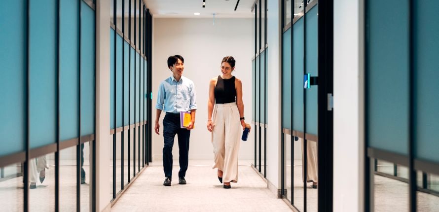 A young man and young woman walk down an office hallway.