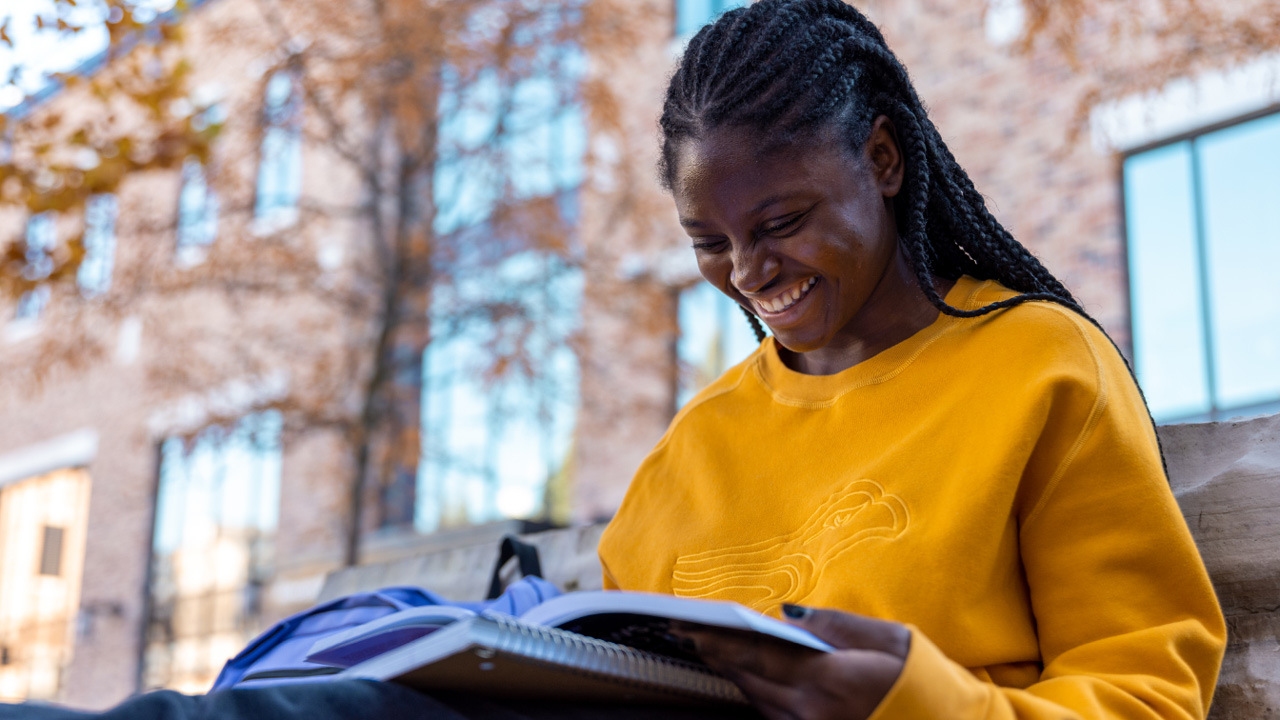 female student in yellow Laurier hoodie smiling down at book